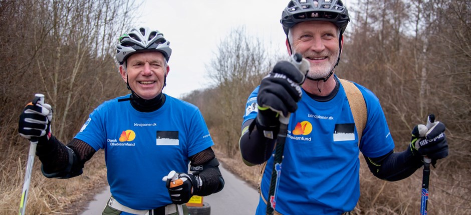 Arne Christensen og hans seende ledsager og ven Claus Geleff træner på rulleski, hvor de trækker bildæk efter sig. 